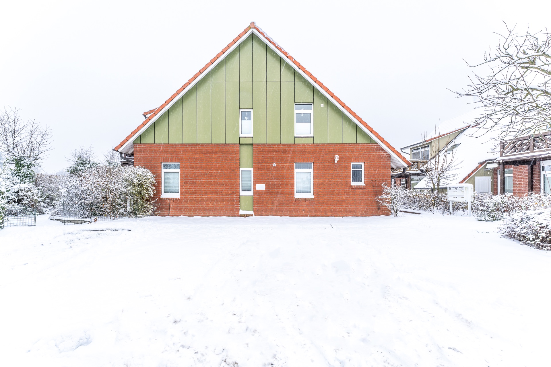 Ein zweistöckiges Haus mit rotem Ziegeldach und verschneitem Garten im Winter.