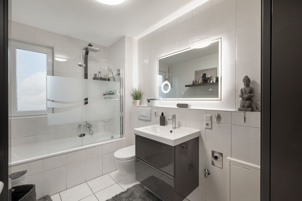 Modernes Badezimmer mit Badewanne, großem Spiegel, Waschbecken und Toilette.