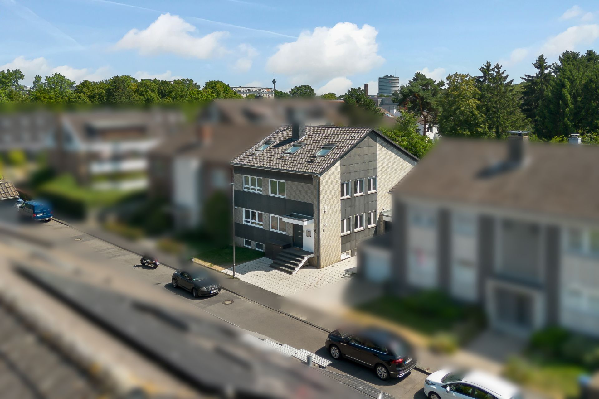Mehrfamilienhaus mit grauer Fassade und Treppe am Eingang, Autos parken auf der Straße davor.