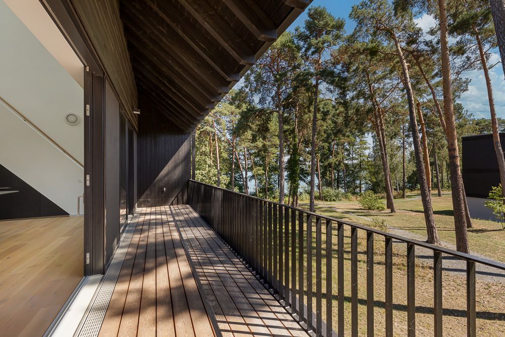 Holzbalkon mit schwarzem Geländer, Blick auf Bäume und Rasenfläche, Zugang von Innenraum.