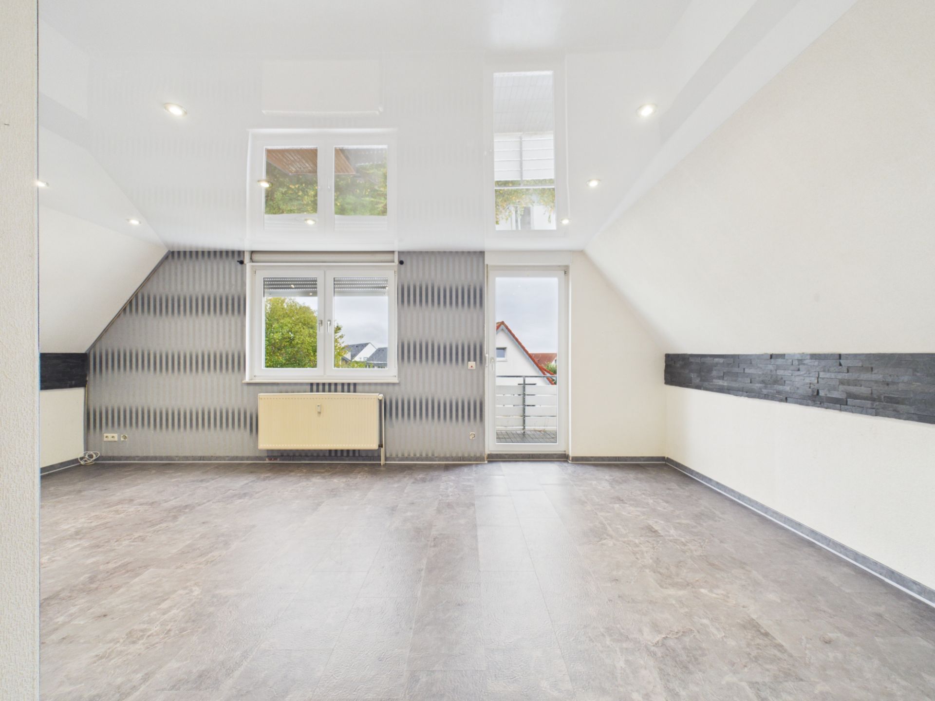 Leerer, heller Raum mit großen Fenstern, Heizkörper und Zugang zu einem Balkon.
