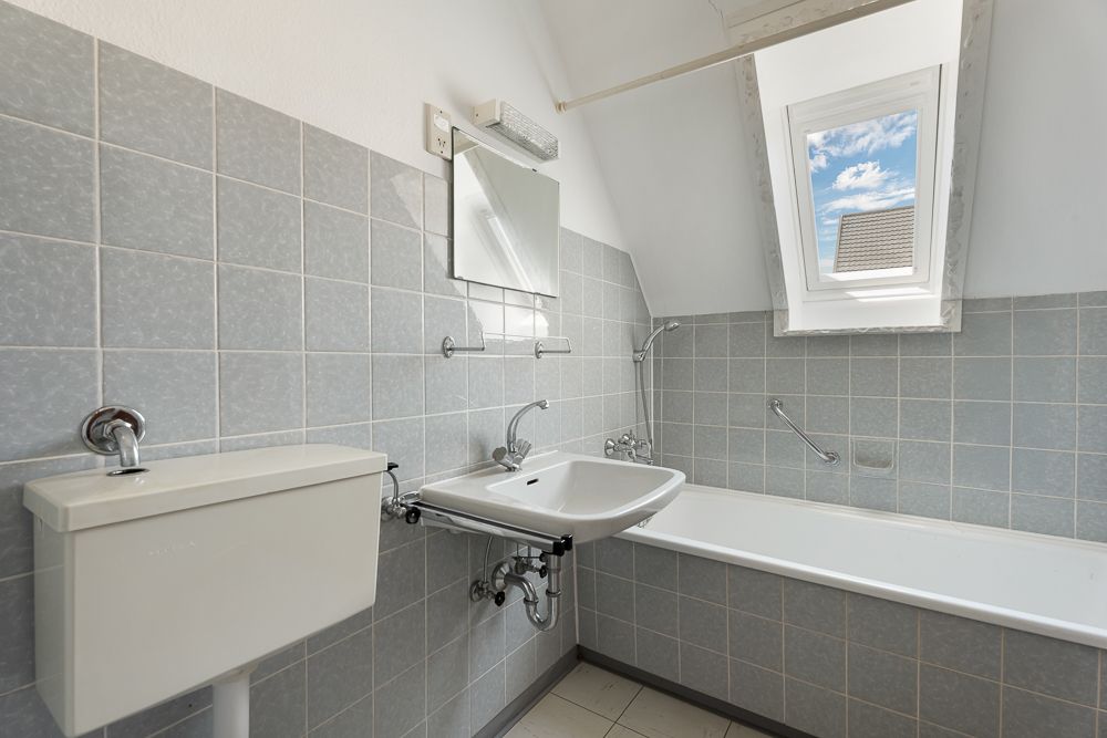 Helles Badezimmer mit Badewanne, Waschbecken, Spiegel, WC und Fenster im Dach.