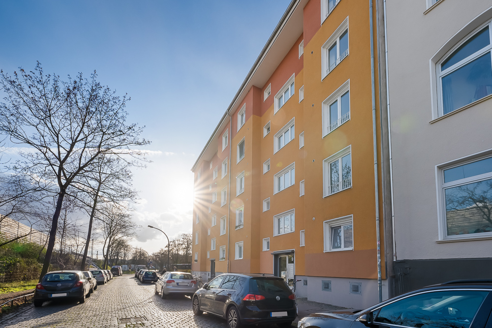 Mehrfamilienhaus mit orangefarbener Fassade und parkenden Autos entlang der Straße.
