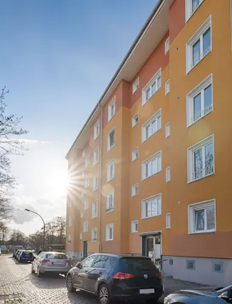Mehrfamilienhaus mit orangefarbener Fassade und parkenden Autos entlang der Straße.