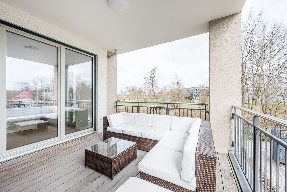 Überdachter Balkon mit Rattansofa, Glastisch und Blick ins Grüne.