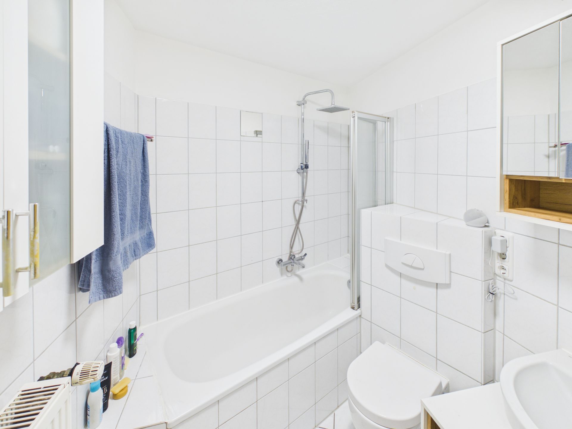 Helles Badezimmer mit Badewanne, Duschkopf, Toilette und weißen Fliesen.