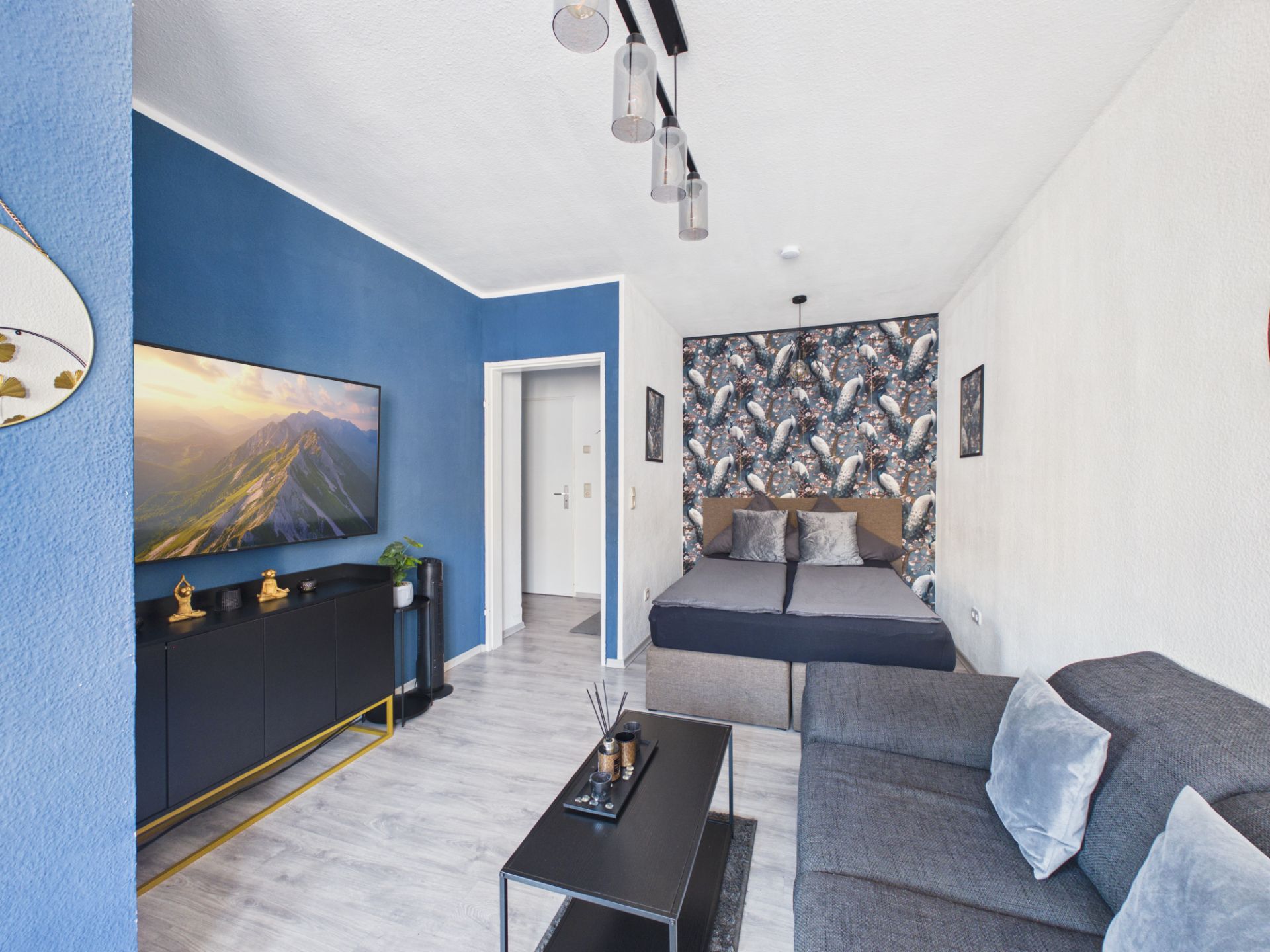 Modernes Wohn-Schlafzimmer mit Bett, Sofa, blau gestrichener Wand und TV.