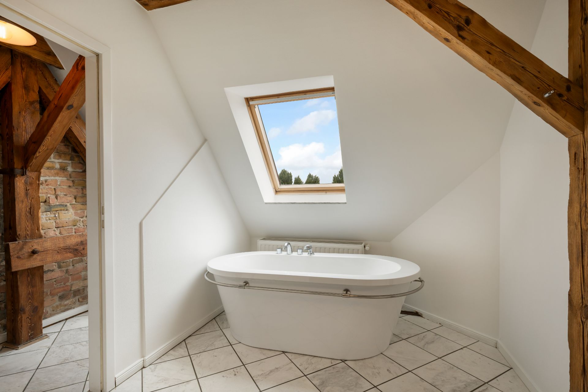 Badezimmer mit freistehender Badewanne und Dachfenster, sichtbare Holzbalken.
