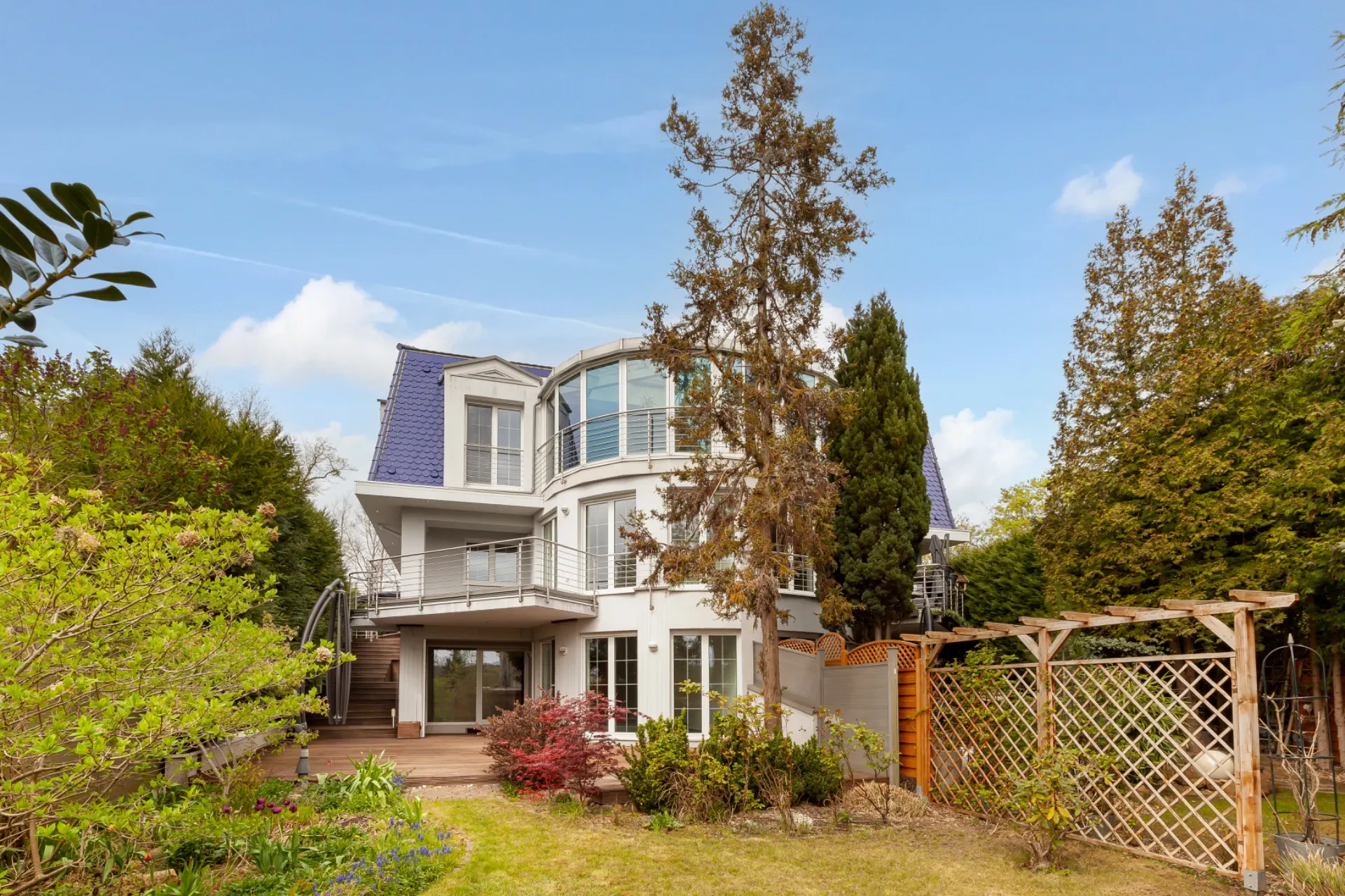 Modernes Wohnhaus mit großem Garten, mehreren Balkonen und umgeben von Bäumen.