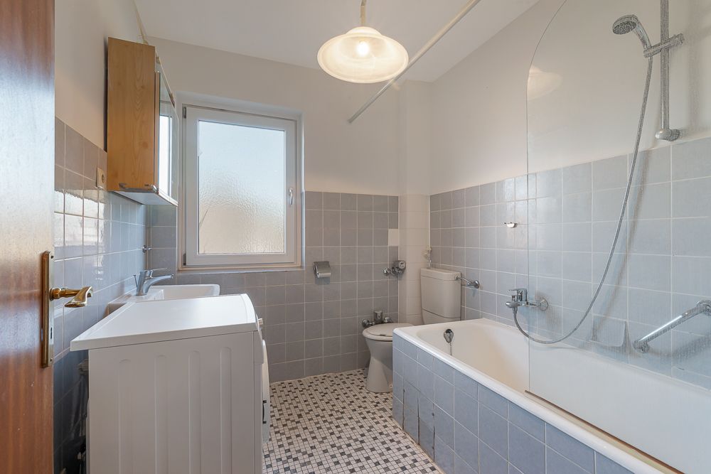Helles Badezimmer mit Badewanne, Waschmaschine, Waschbecken, WC und Fenster.
