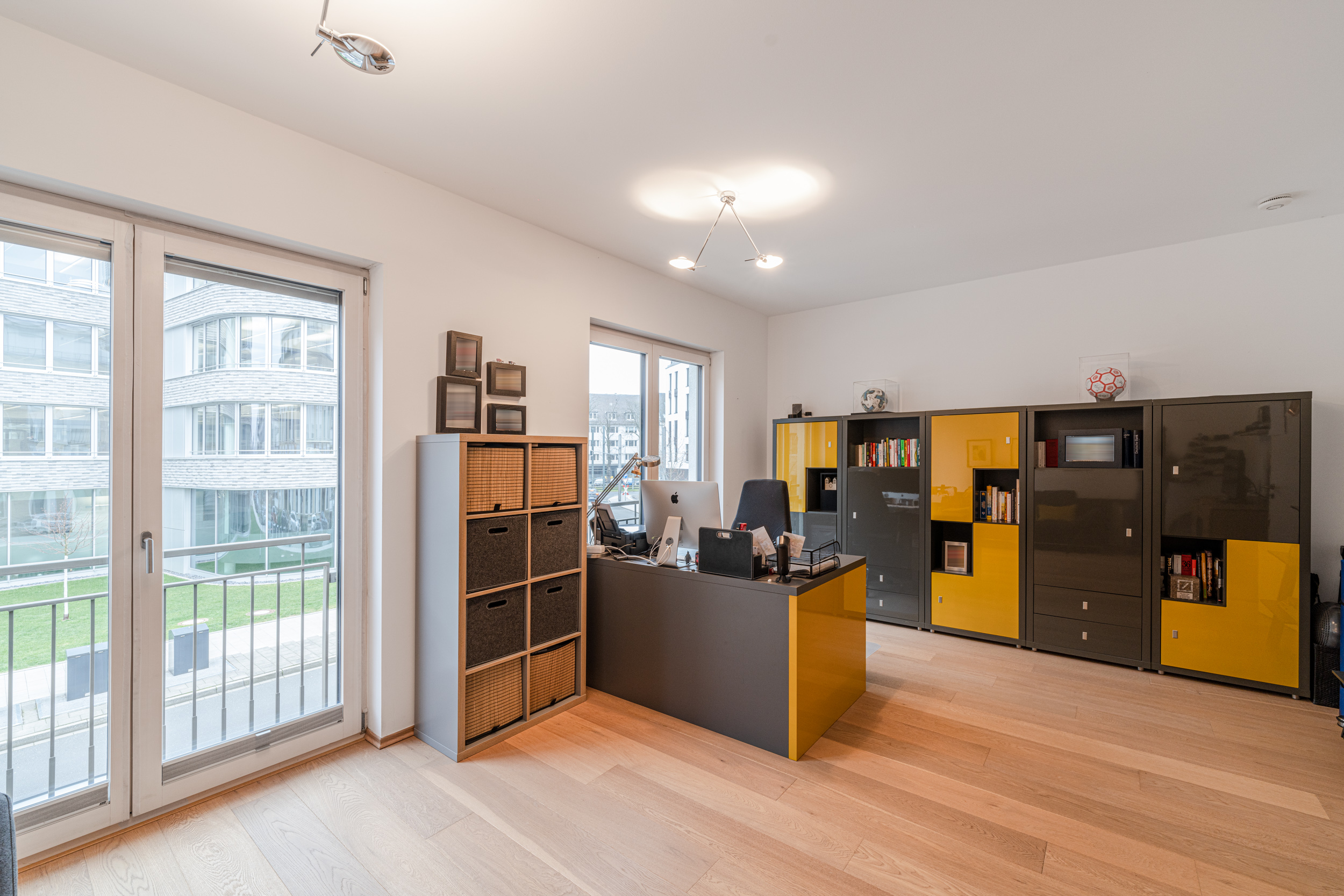 Modernes Arbeitszimmer mit großem Schreibtisch, Regalen und Blick auf große Fenster.
