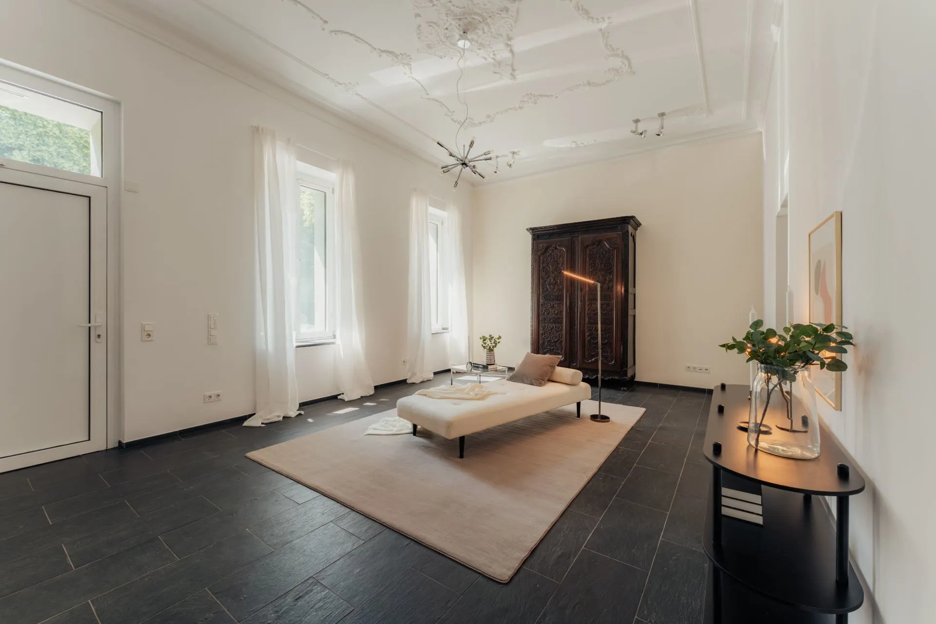Helles Wohnzimmer mit dunklem Boden, Sofa, Teppich, großem Schrank und Dekoration.