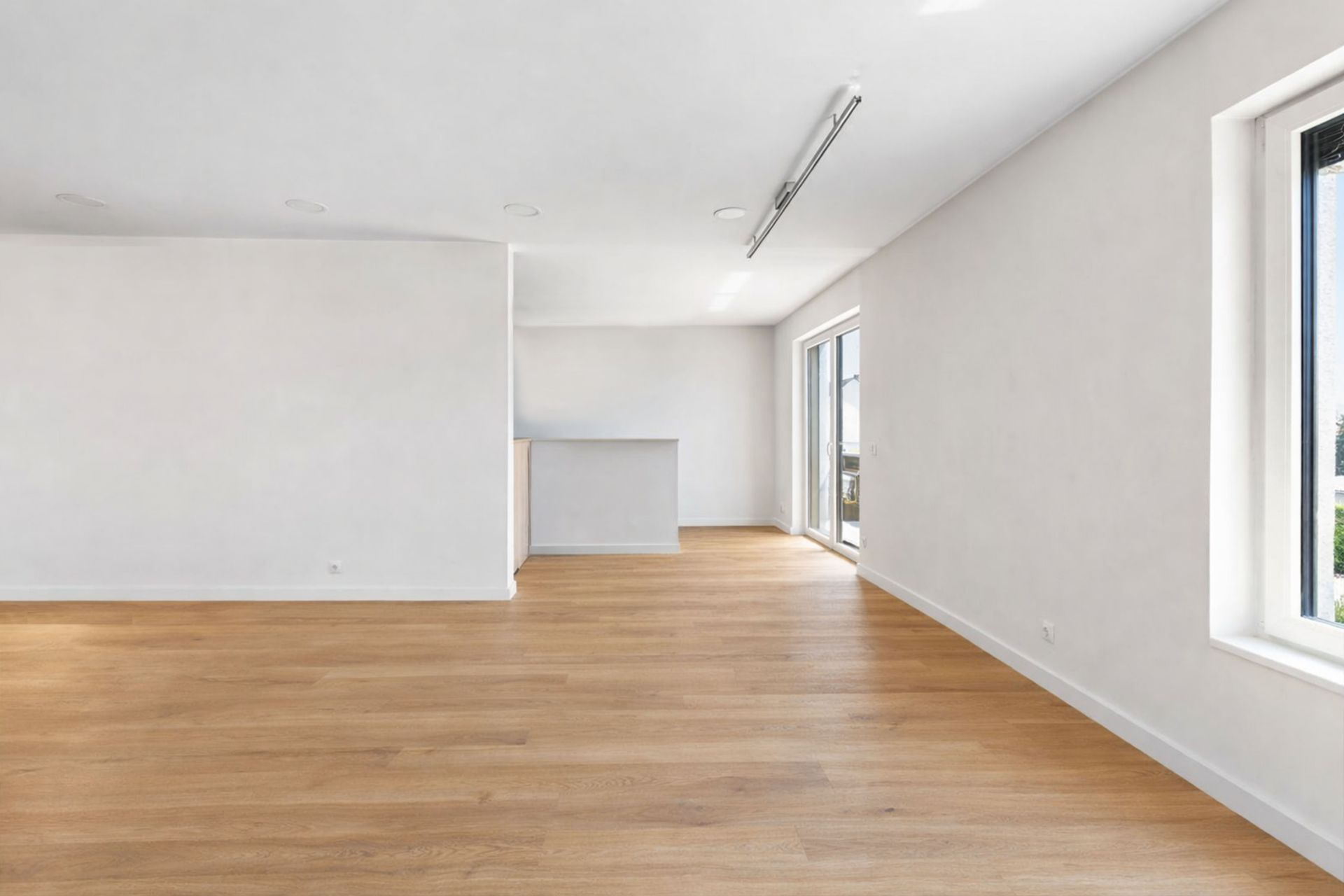 Heller, leerer Raum mit Holzfußboden, weißen Wänden und großen Fenstern.