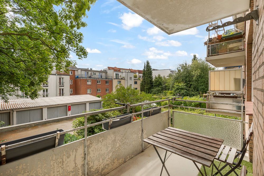 Balkon mit Holztisch und Stühlen, Blick auf Bäume und benachbarte Wohngebäude.