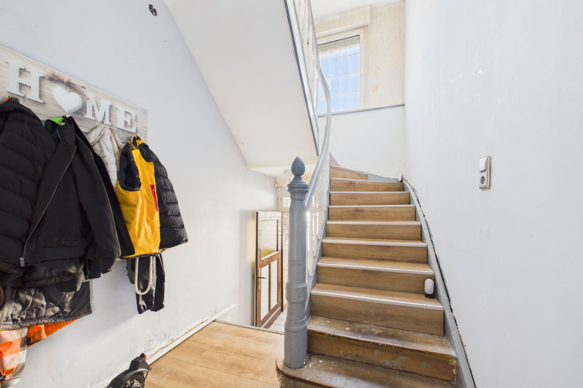 Holztreppe mit Handlauf in einem Flur, links Garderobe mit Jacken an Haken.