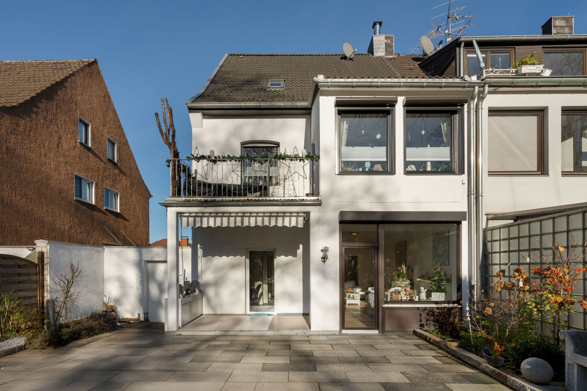 Zweistöckiges Wohnhaus mit Balkon und großem Fenster im Erdgeschoss, gepflasterter Hof davor.