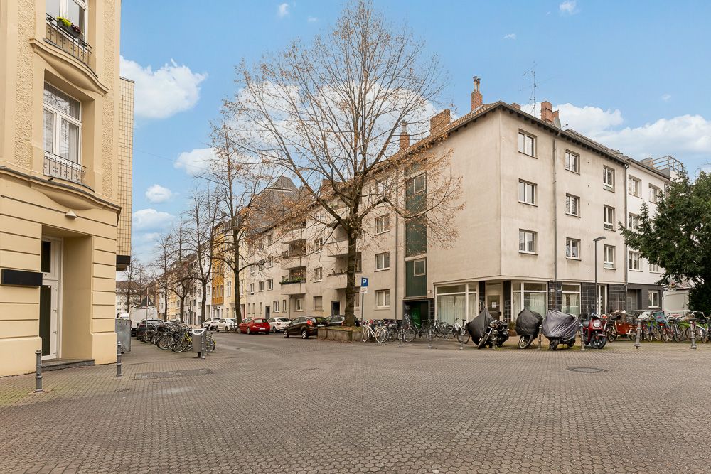 Wohnhaus an einer Straßenecke mit Fahrrädern, Motorrädern und Bäumen davor.