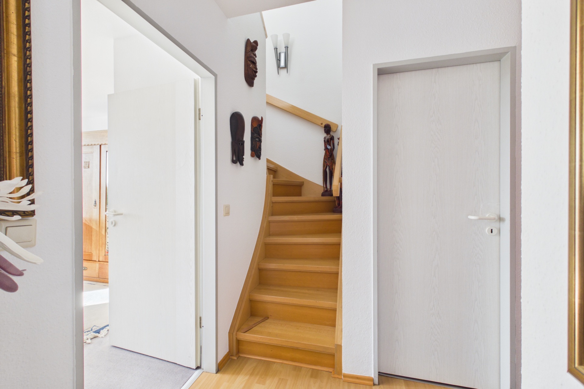 Holztreppe mit weißen Türen und Wanddekorationen in einem Flur eines Wohnhauses.