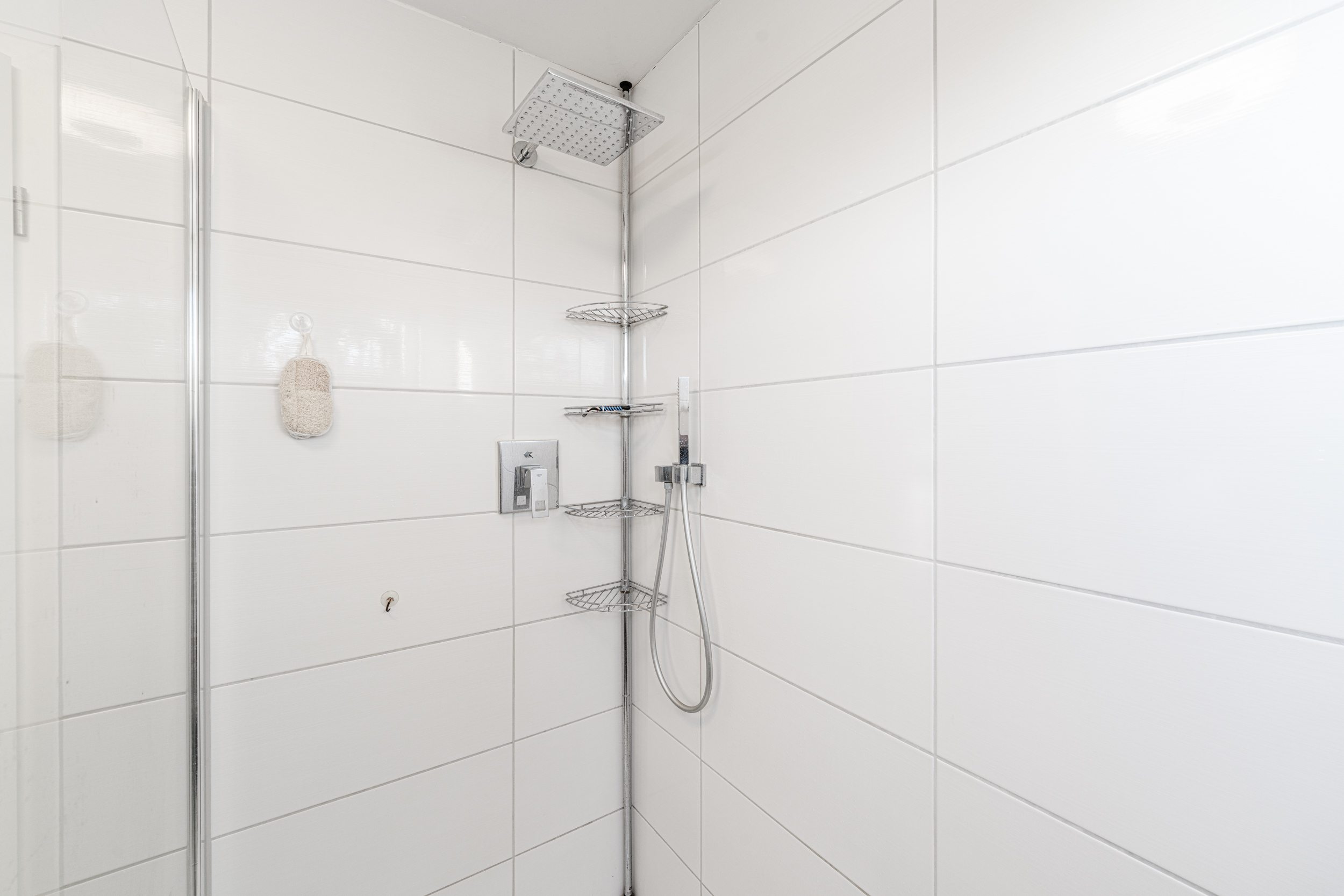Moderne Dusche mit weiß gefliesten Wänden, Regenduschkopf und Eckregal aus Metall.