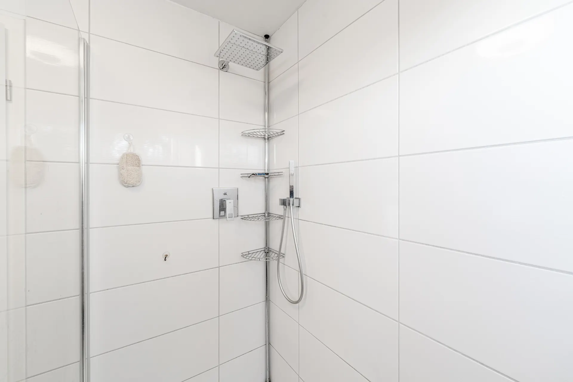 Moderne Dusche mit weiß gefliesten Wänden, Regenduschkopf und Eckregal aus Metall.