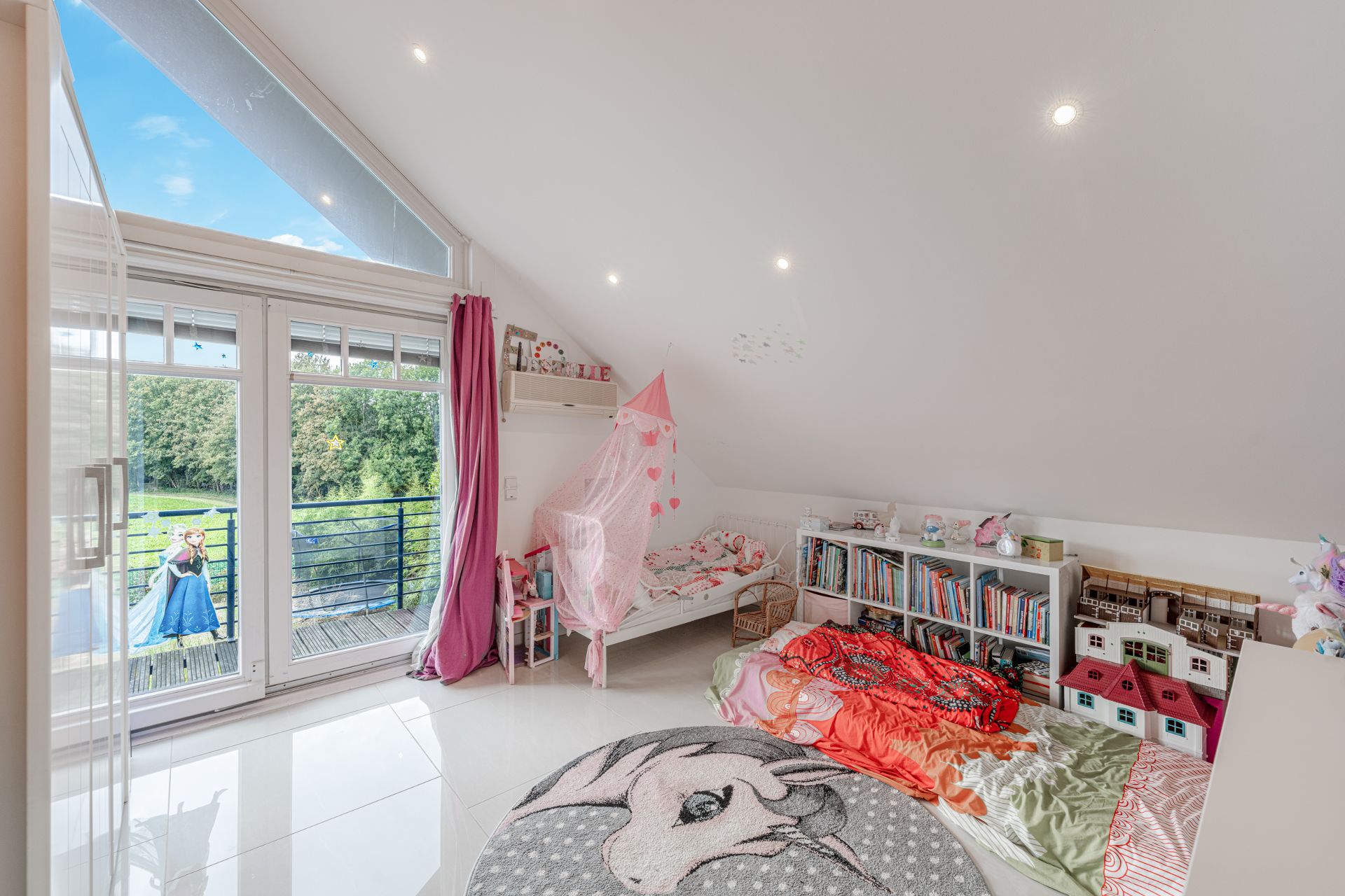 Helles Kinderzimmer mit Bett, Bücherregalen, Spielzeughaus und Zugang zum Balkon.