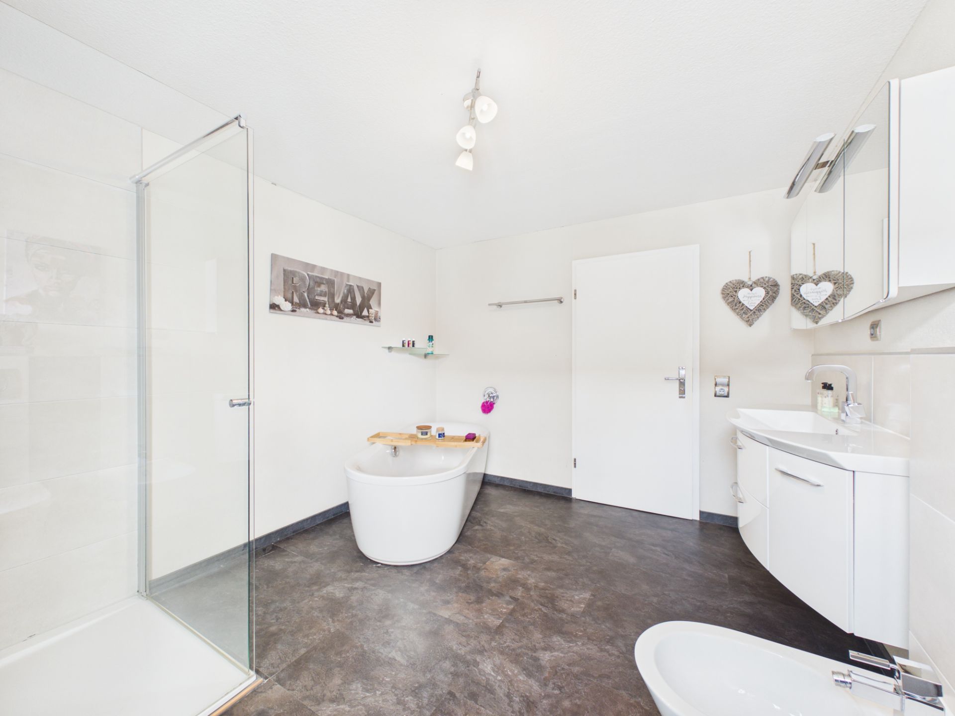 Modernes Badezimmer mit freistehender Badewanne, Dusche, Waschbecken und Dekoration an der Wand.