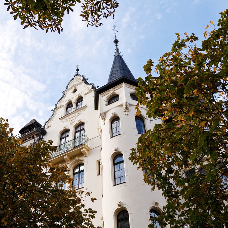 Historisches Wohngebäude mit Turm und großen Fenstern, von Bäumen umgeben.