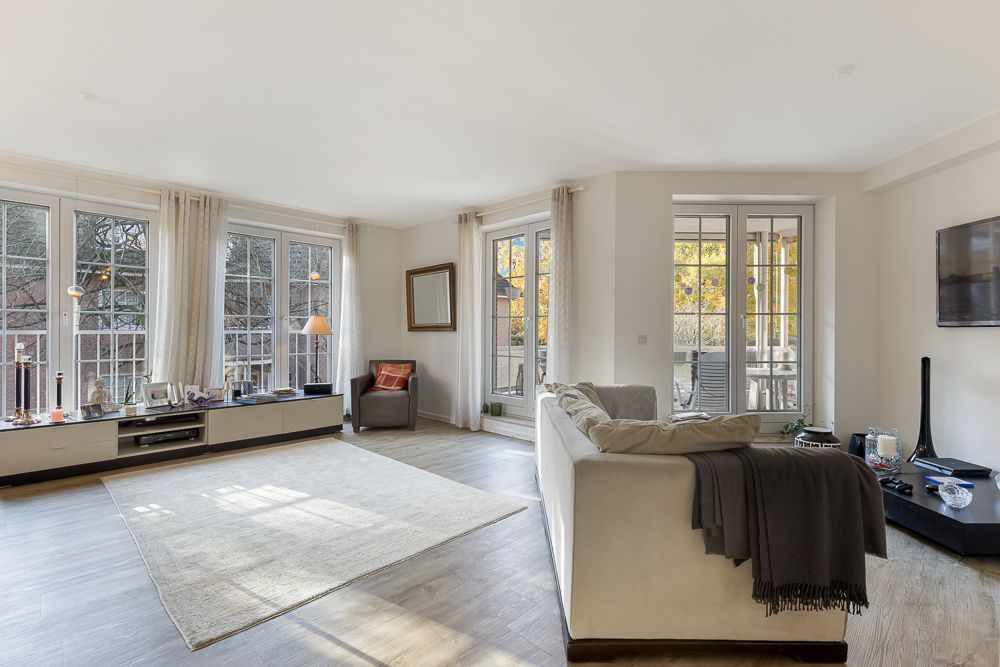 Helles Wohnzimmer mit großen Fenstern, Sofa, Teppich und Sessel.