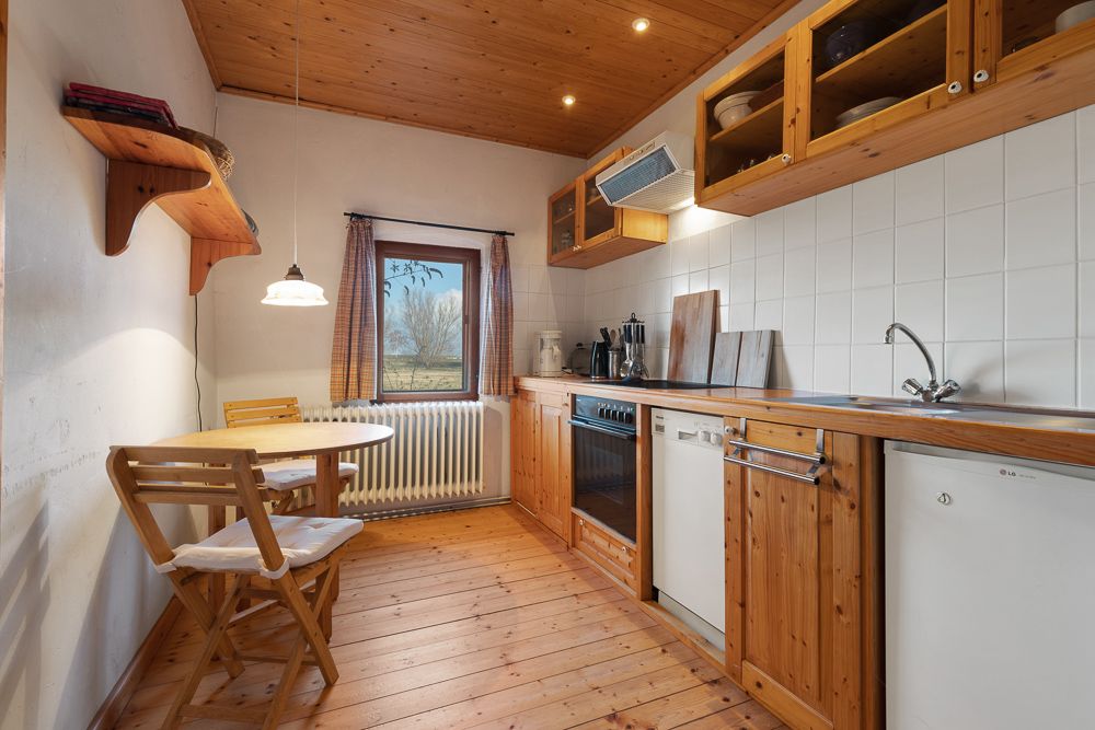 Gemütliche Holzküche mit kleinem Esstisch, Stühlen und Fenster mit Blick nach draußen.
