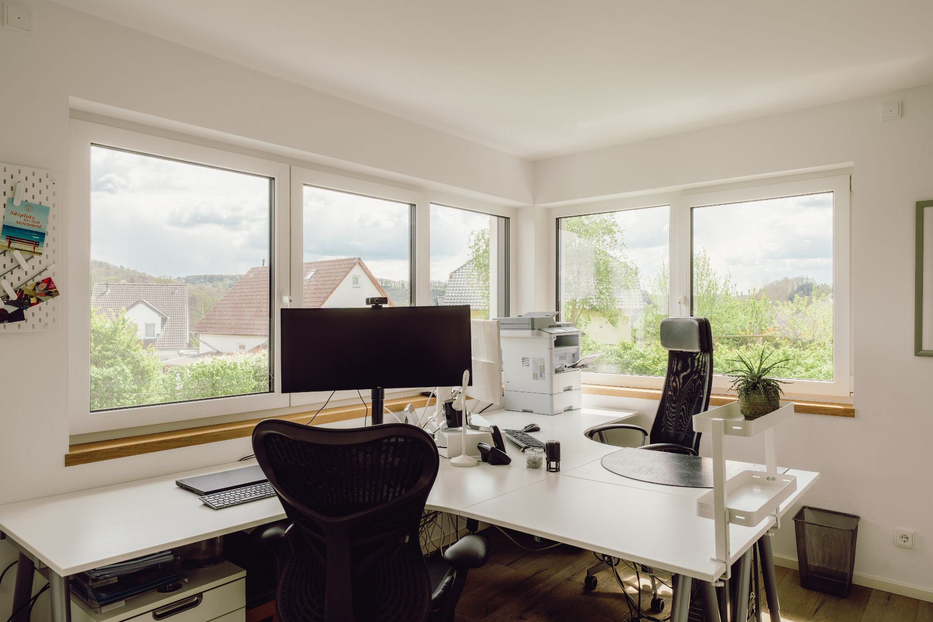 Helles Arbeitszimmer mit großen Fenstern, zwei Schreibtischen, Monitor, Drucker und Bürostuhl.