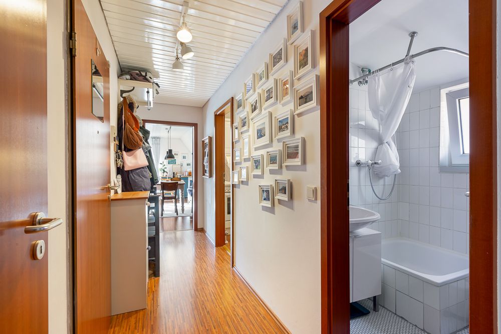 Flur mit Holzboden, vielen Bilderrahmen an der Wand und Blick ins Badezimmer mit Badewanne.