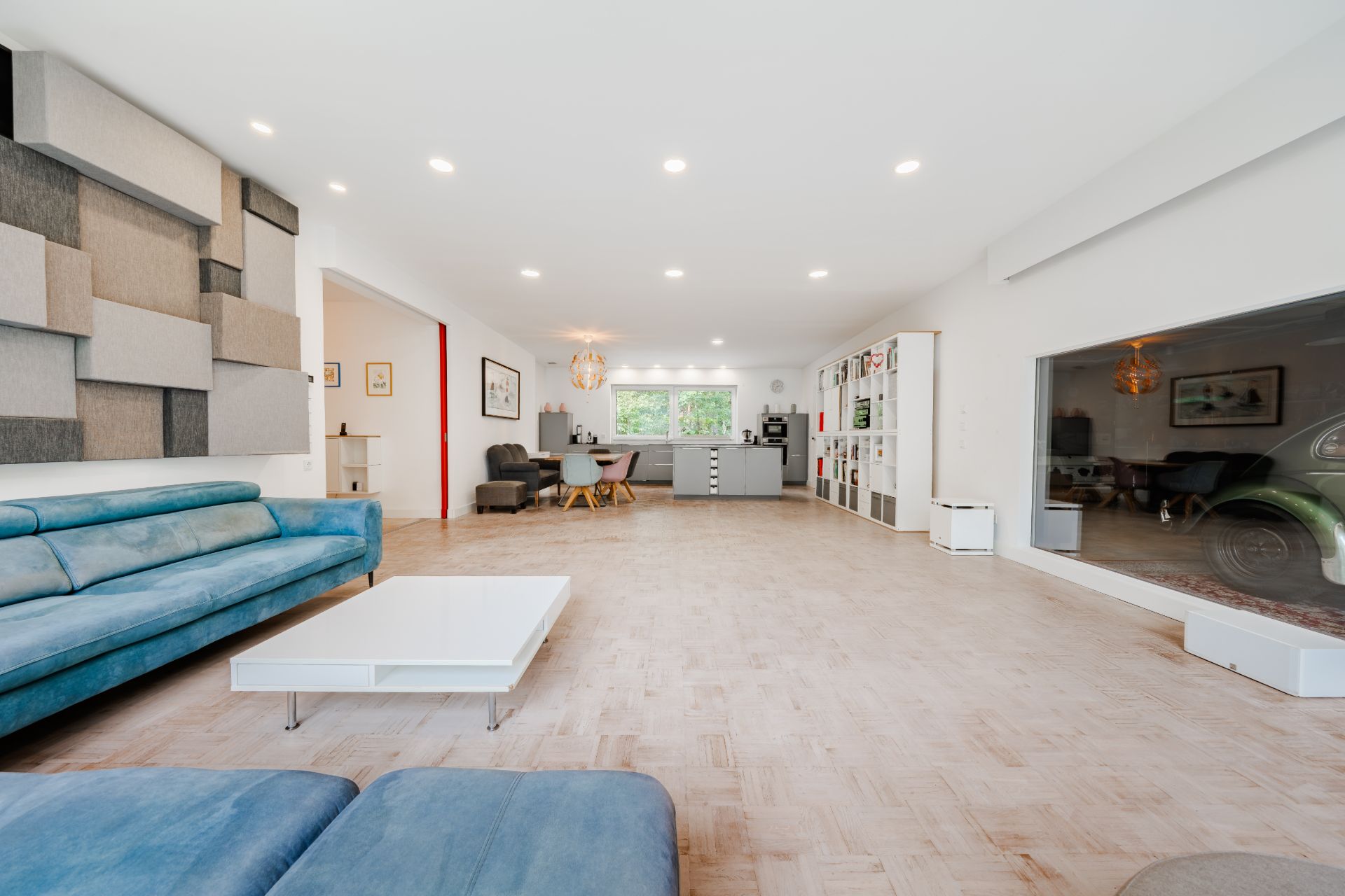 Großes, helles Wohnzimmer mit blauen Sofas, Couchtisch und offener Küche im Hintergrund.