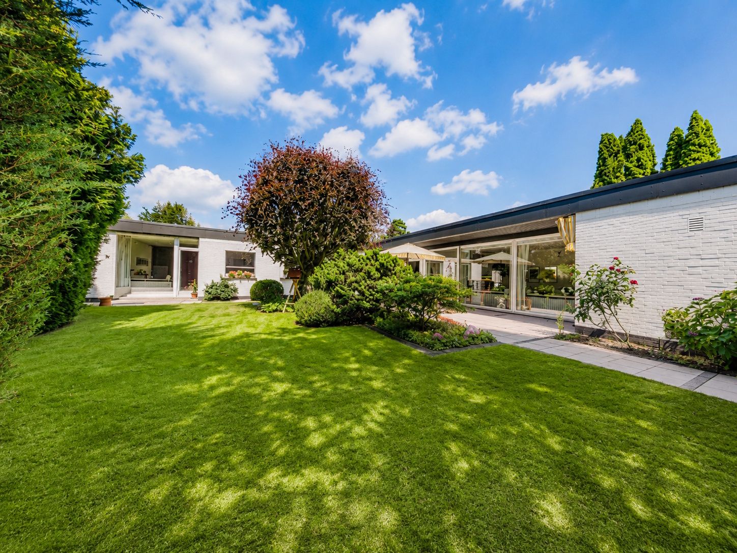 Großer gepflegter Garten mit Rasen, Sträuchern und Bäumen vor einem modernen, weißen Wohnhaus.
