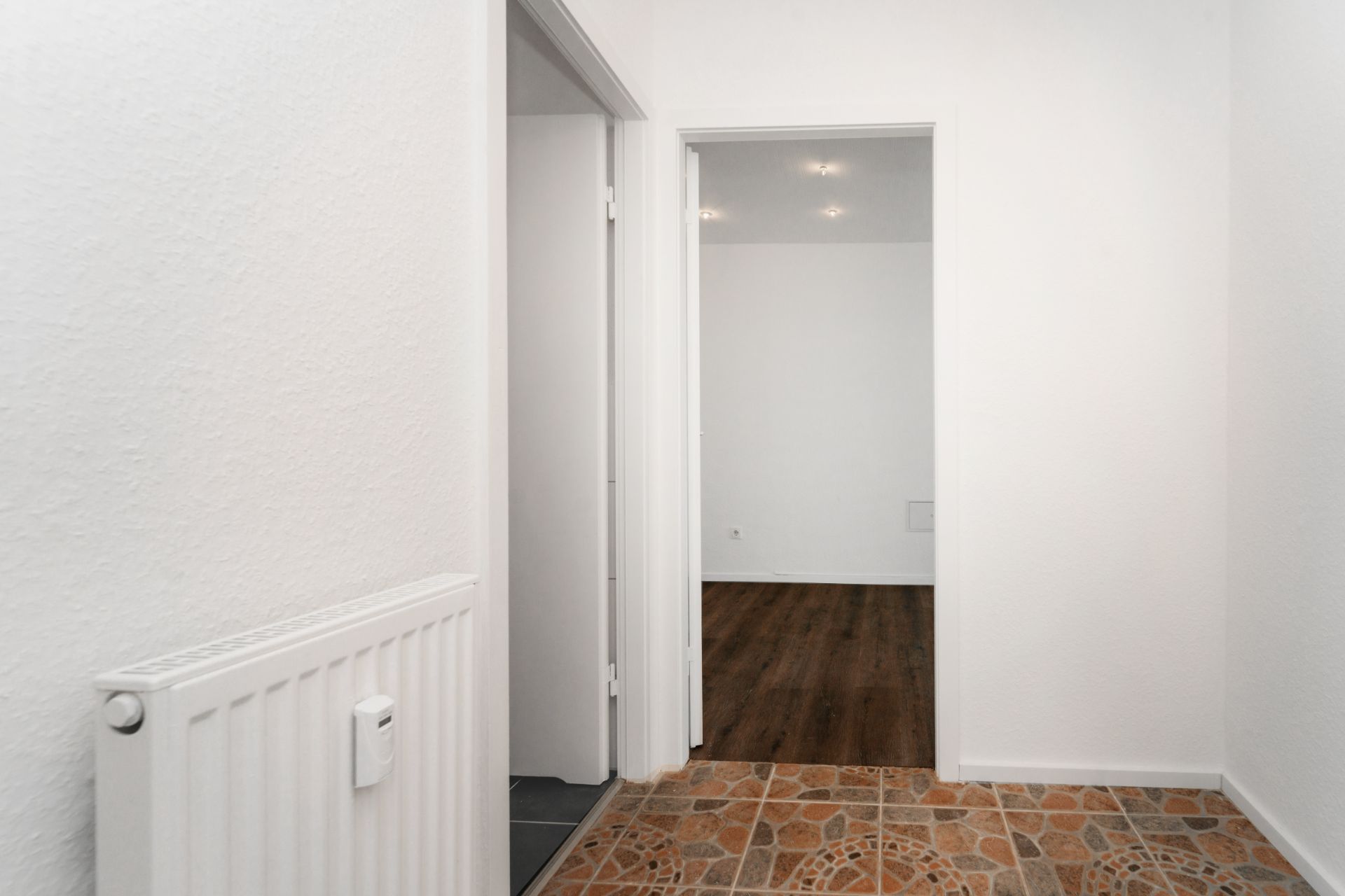 Heller Flur mit Fliesenboden, Heizkörper und Türen zu angrenzenden Räumen.