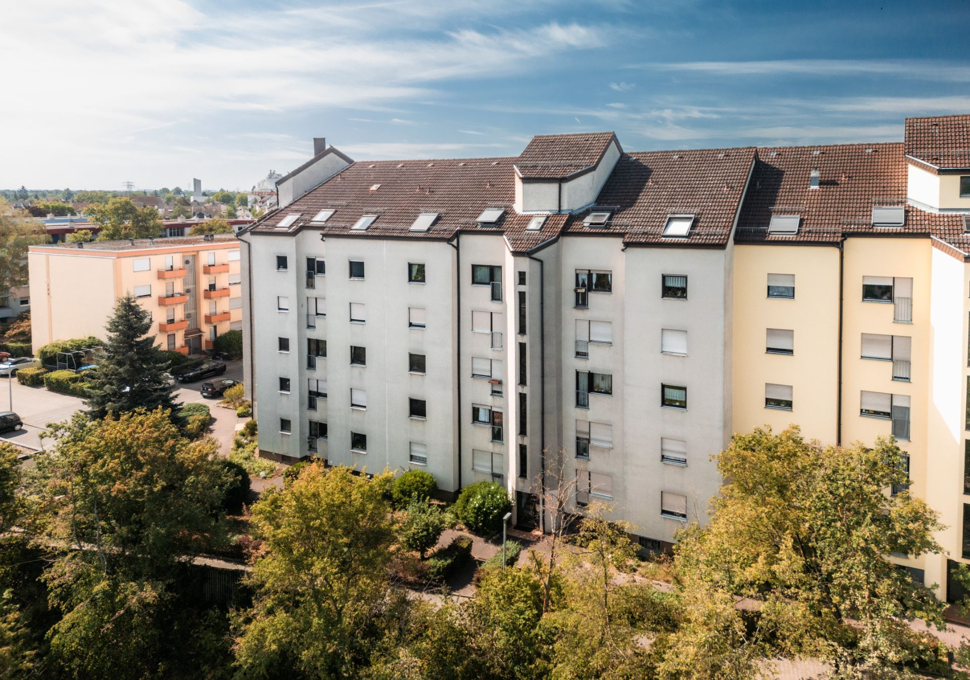 Mehrstöckiges Wohnhaus mit hellen Fassaden und vielen Fenstern, umgeben von Bäumen.
