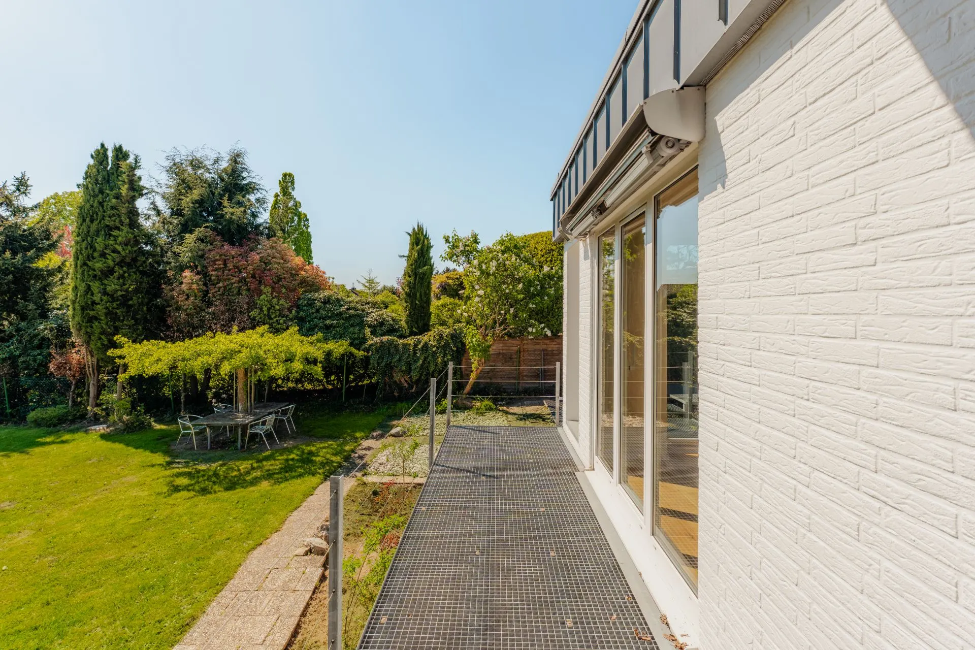 Balkon an einem weißen Haus mit Blick auf einen Garten mit Bäumen und einer Sitzecke.