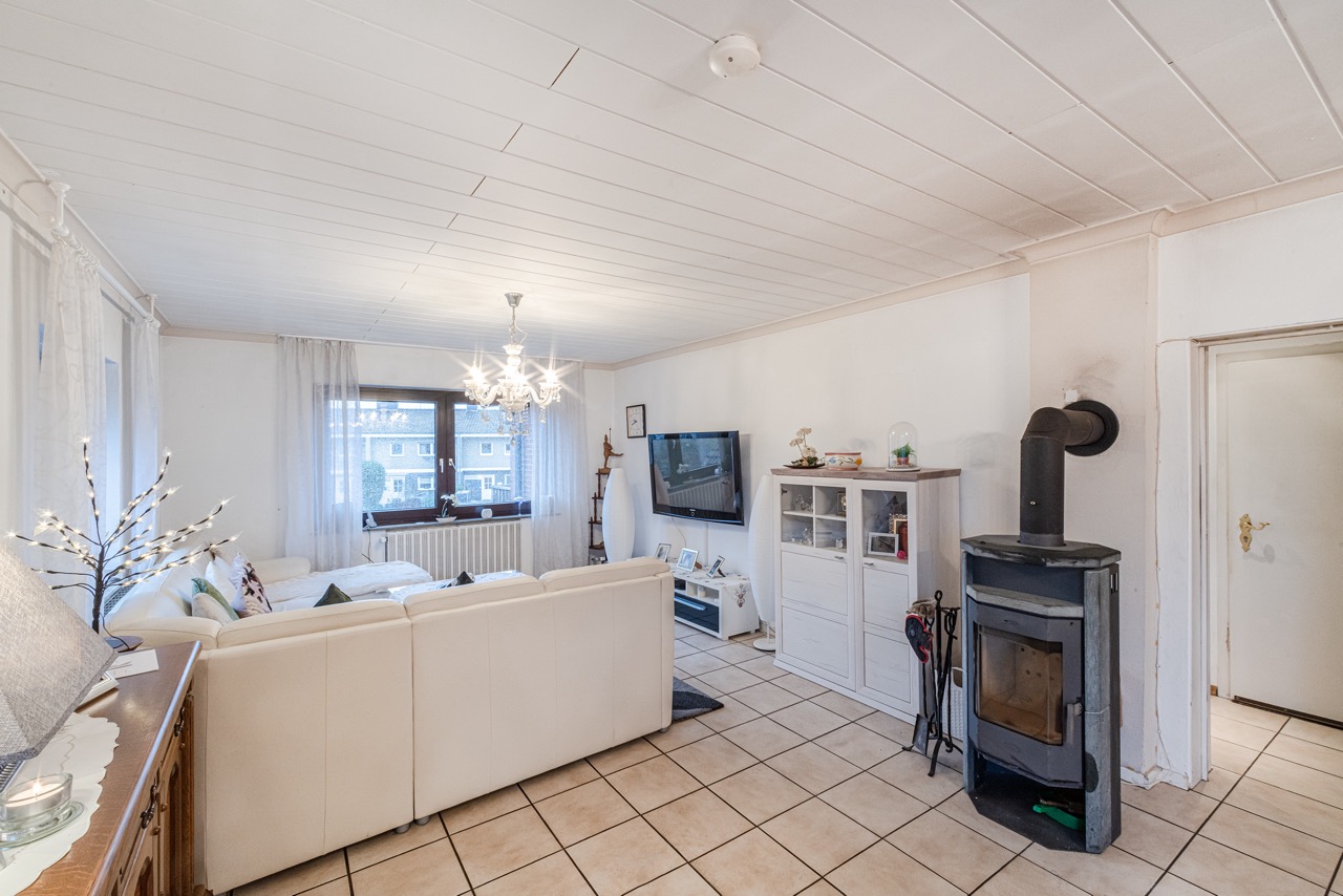 Helles Wohnzimmer mit weißen Sofas, Kaminofen, Fernseher und großem Fenster.