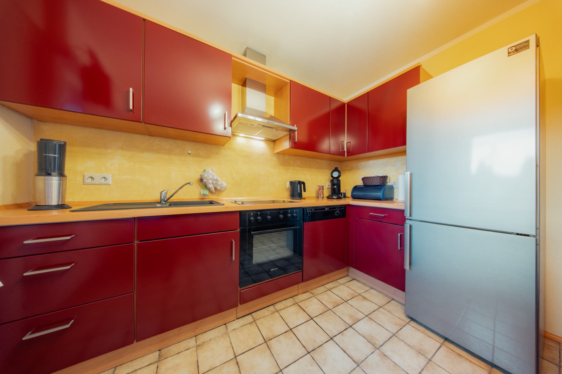 Küche mit roten Schränken, großem Kühlschrank, Herd, Spüle und Kaffeemaschine.