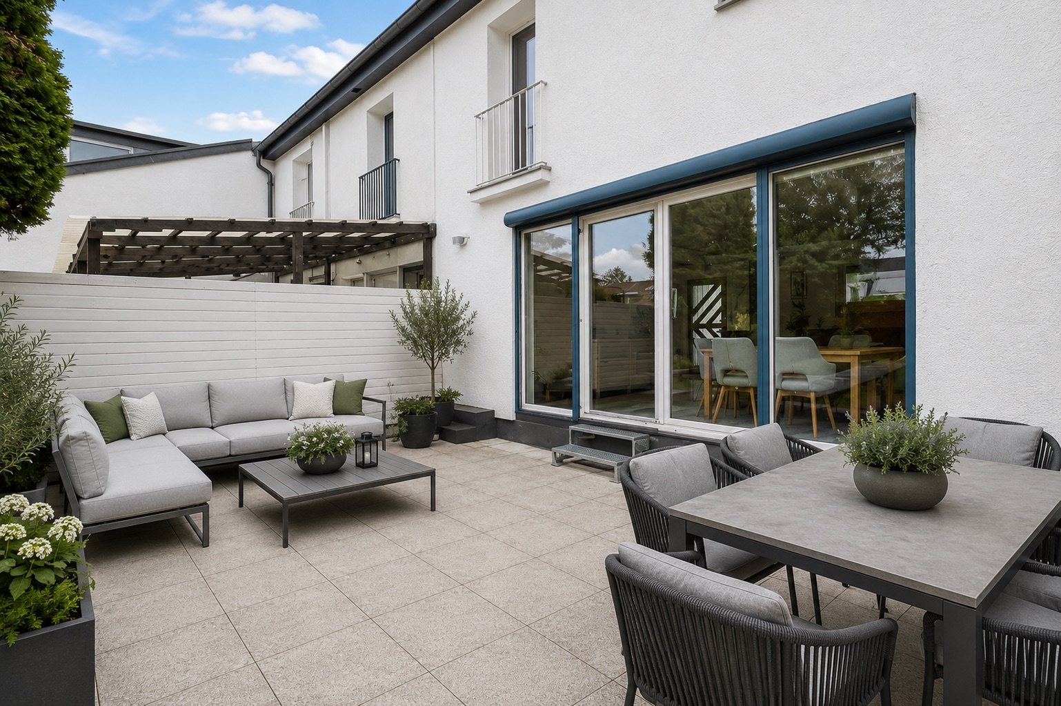 Moderne Terrasse mit Sitzgruppe, Esstisch, Pflanzen und Zugang zum Haus durch große Glasschiebetüren.