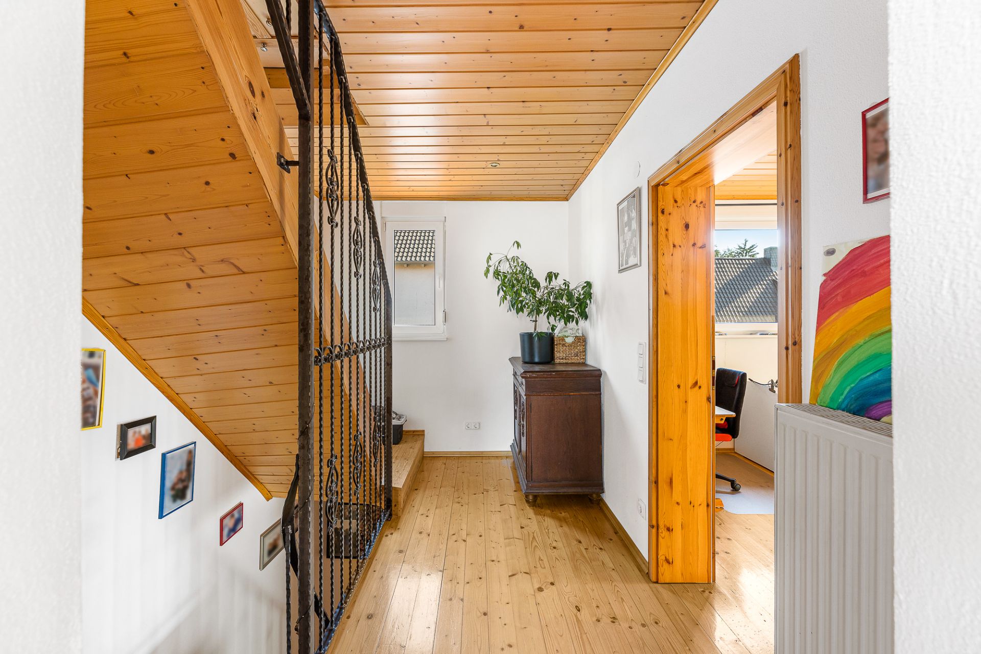 Flur mit Holzdecke, Treppe, Kommode mit Pflanze und Durchgang zu einem bunten Zimmer.