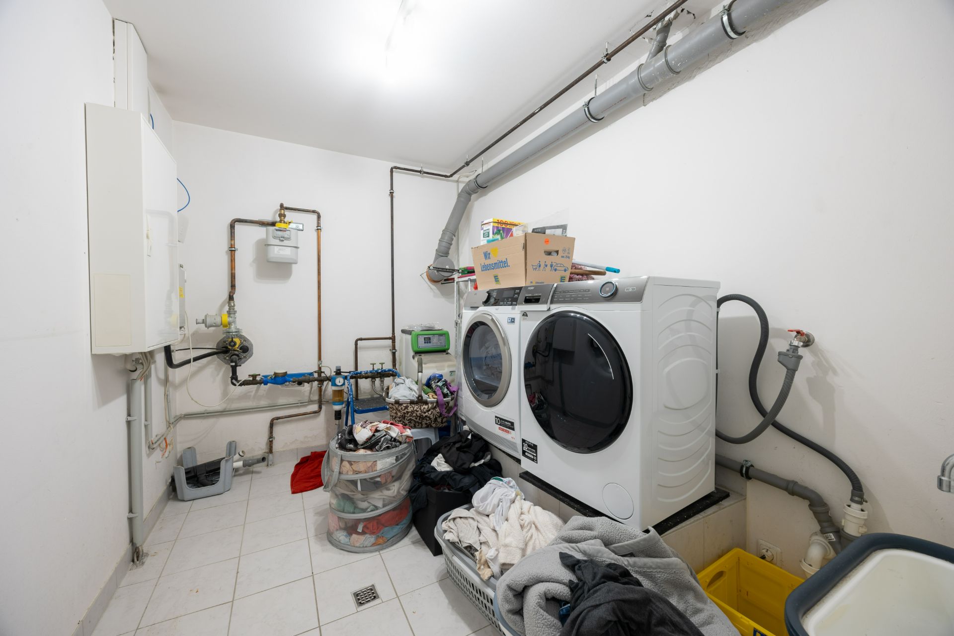 Hauswirtschaftsraum mit Waschmaschine, Trockner und mehreren Wäschekörben voller Kleidung.