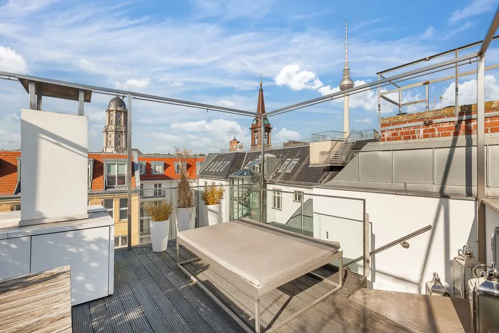 Moderne Dachterrasse mit Sitzbereich, Pflanzen und Stadtblick bei blauem Himmel.