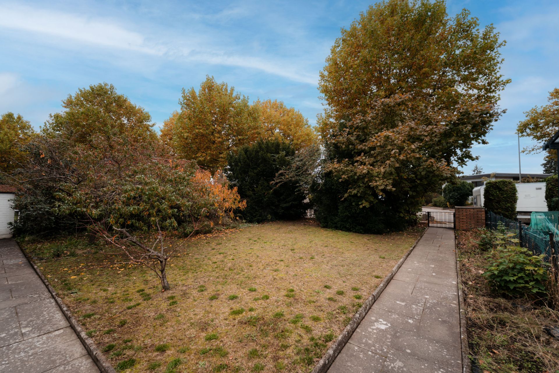 Garten mit Rasenfläche, Bäumen und zwei seitlichen Gehwegen.