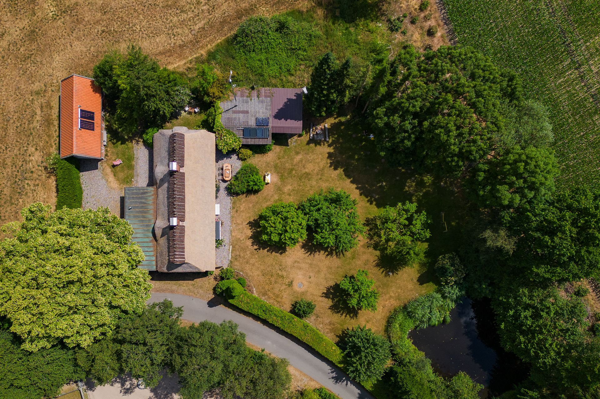 Luftaufnahme eines Hauses mit Nebengebäude, großem Garten, Bäumen und Teich.