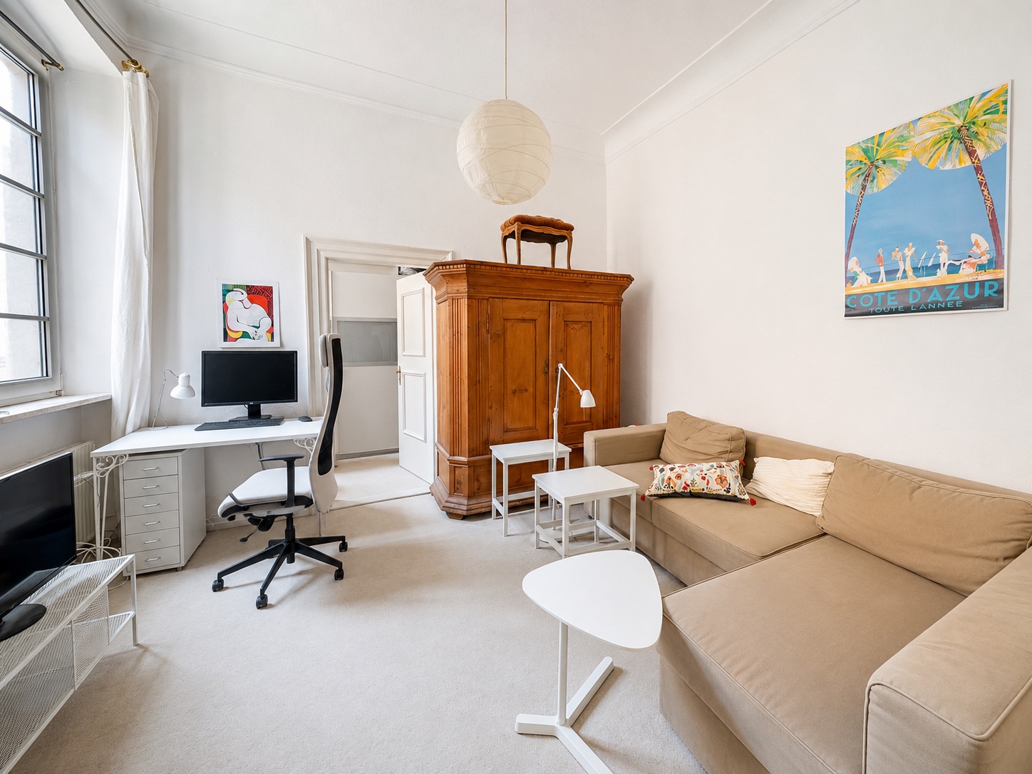 Helles Wohnzimmer mit Ecksofa, Schreibtisch, Holzschrank und großen Fenstern.