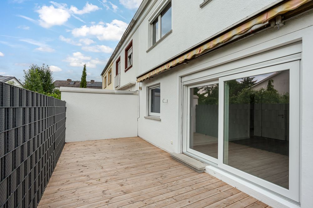 Holzterrasse an einem weißen Wohnhaus mit großen Glastüren und Sichtschutzzaun.