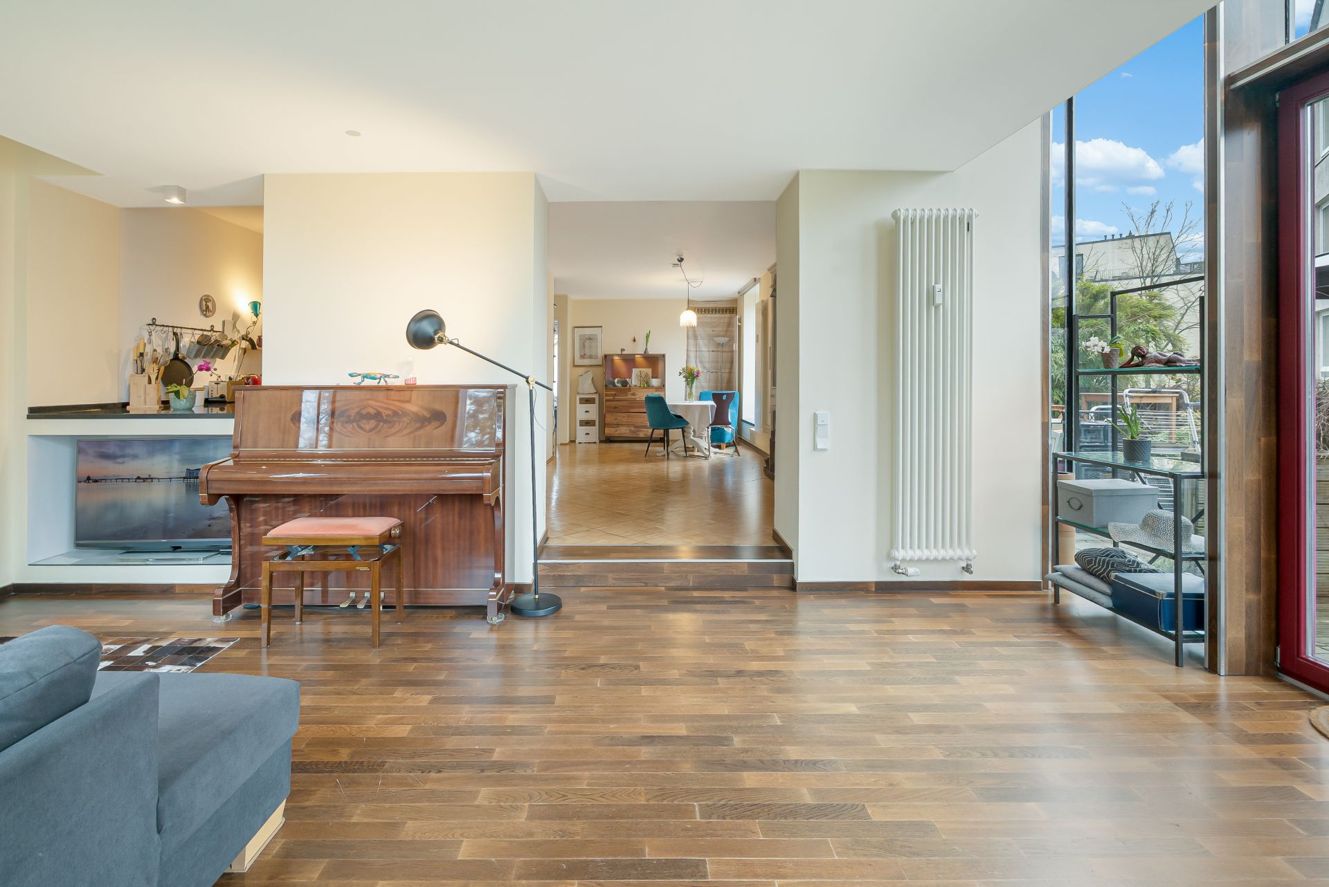 Wohnzimmer mit Holzfußboden, Klavier, Stehlampe und Blick ins Esszimmer.
