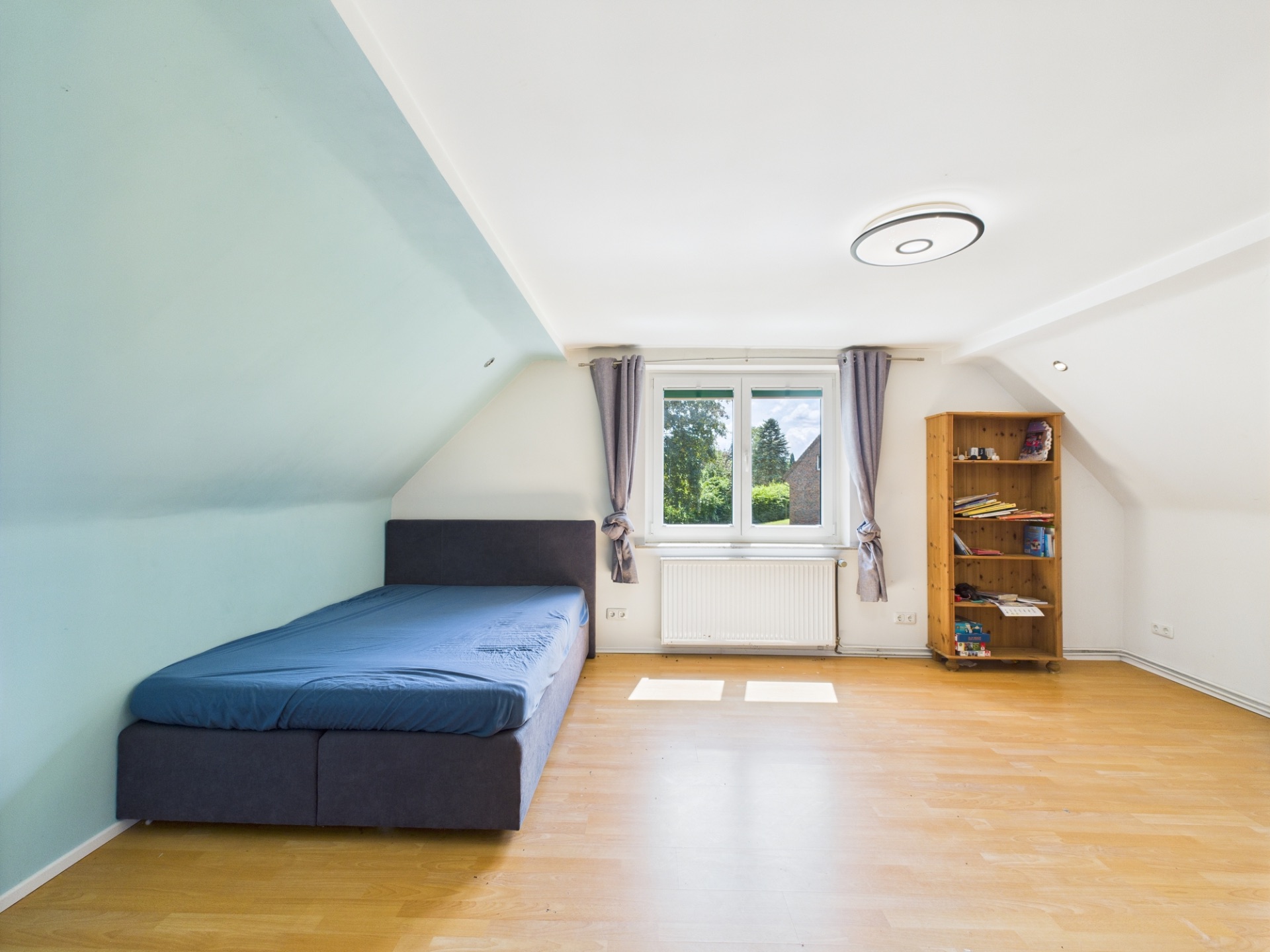 Helles Schlafzimmer mit Einzelbett, Fenster mit Vorhängen und Regal auf Holzfußboden.