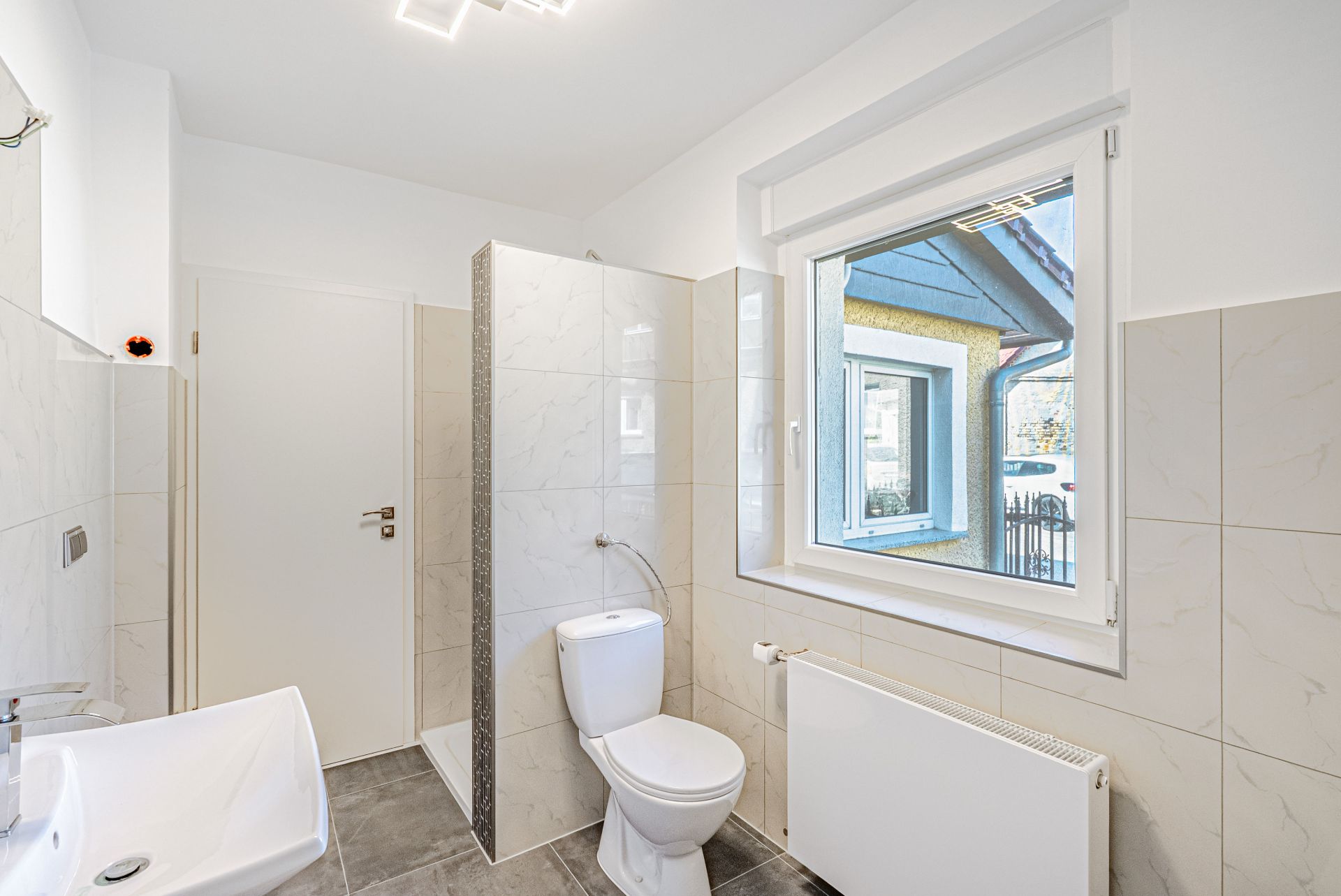 Modernes Badezimmer mit WC, Waschbecken, Dusche und großem Fenster.