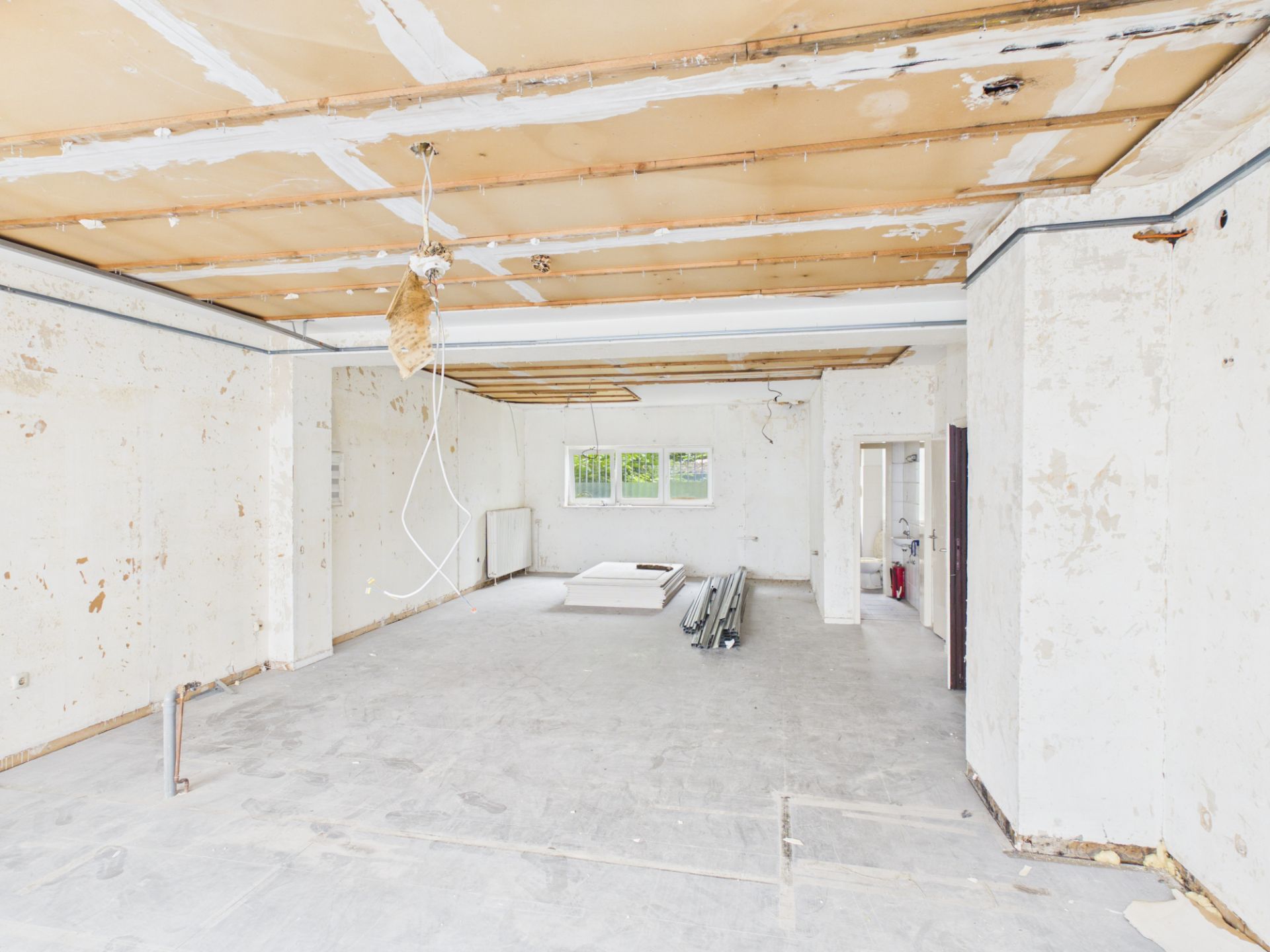 Großer leerer Raum in Renovierung mit offenliegender Decke und Baumaterial auf dem Boden.